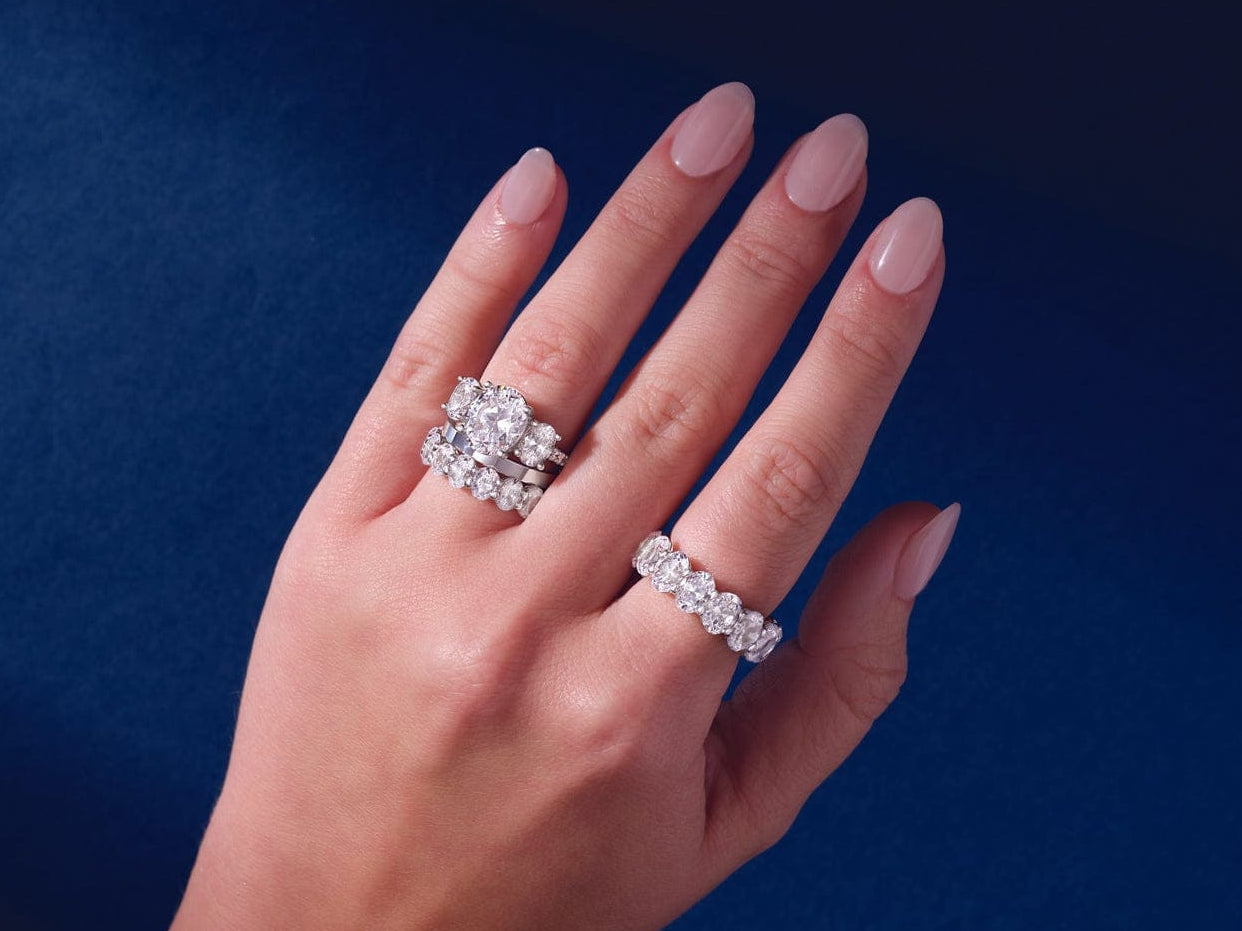 Hand wearing two diamond anniversary rings on a dark blue background