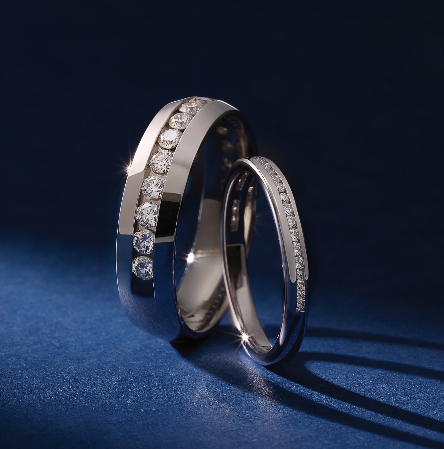 Two polished white gold wedding bands with channel-set diamonds showcased on a dark blue surface during a personalized consultation.