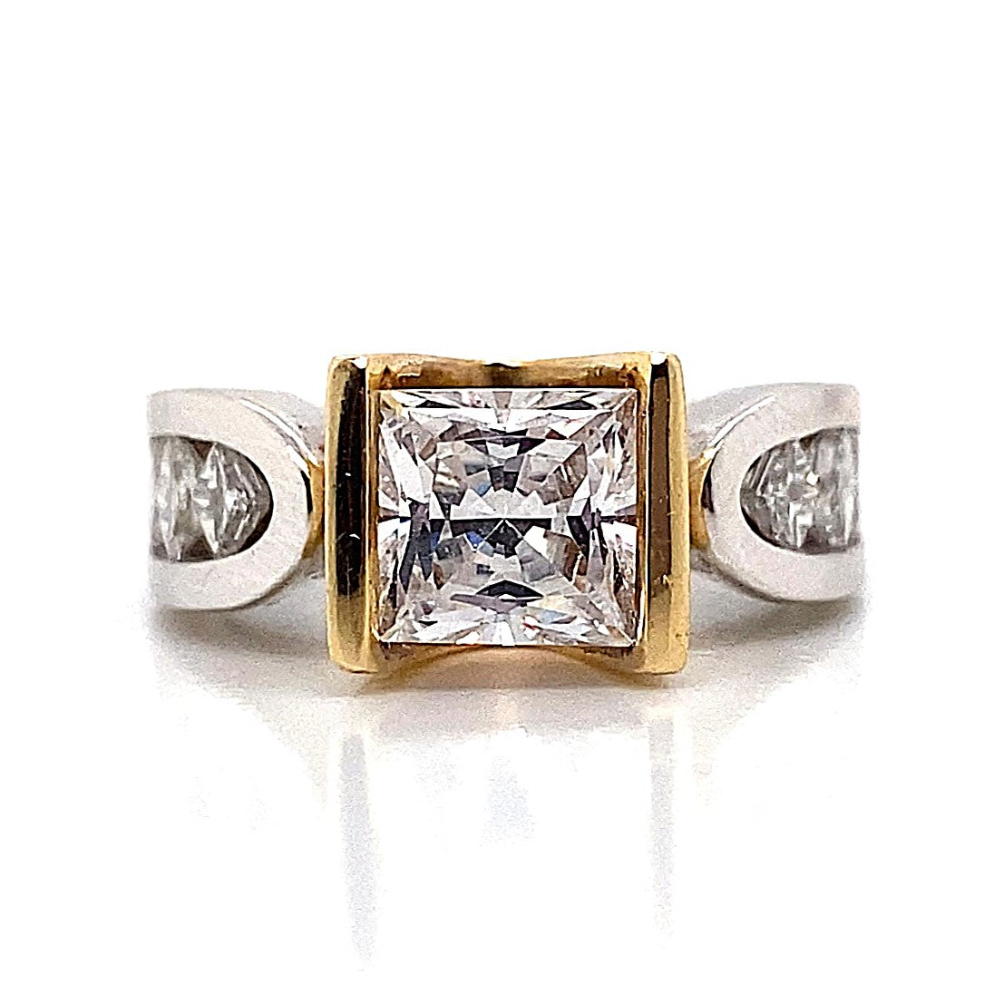 A striking piece of jewelry, the 14K white and yellow gold V-channel head ring showcases a 6.5mm princess-cut CZ centerpiece, accented by .75 carat total weight natural princess diamond accents along the square shank for an added touch of elegance.