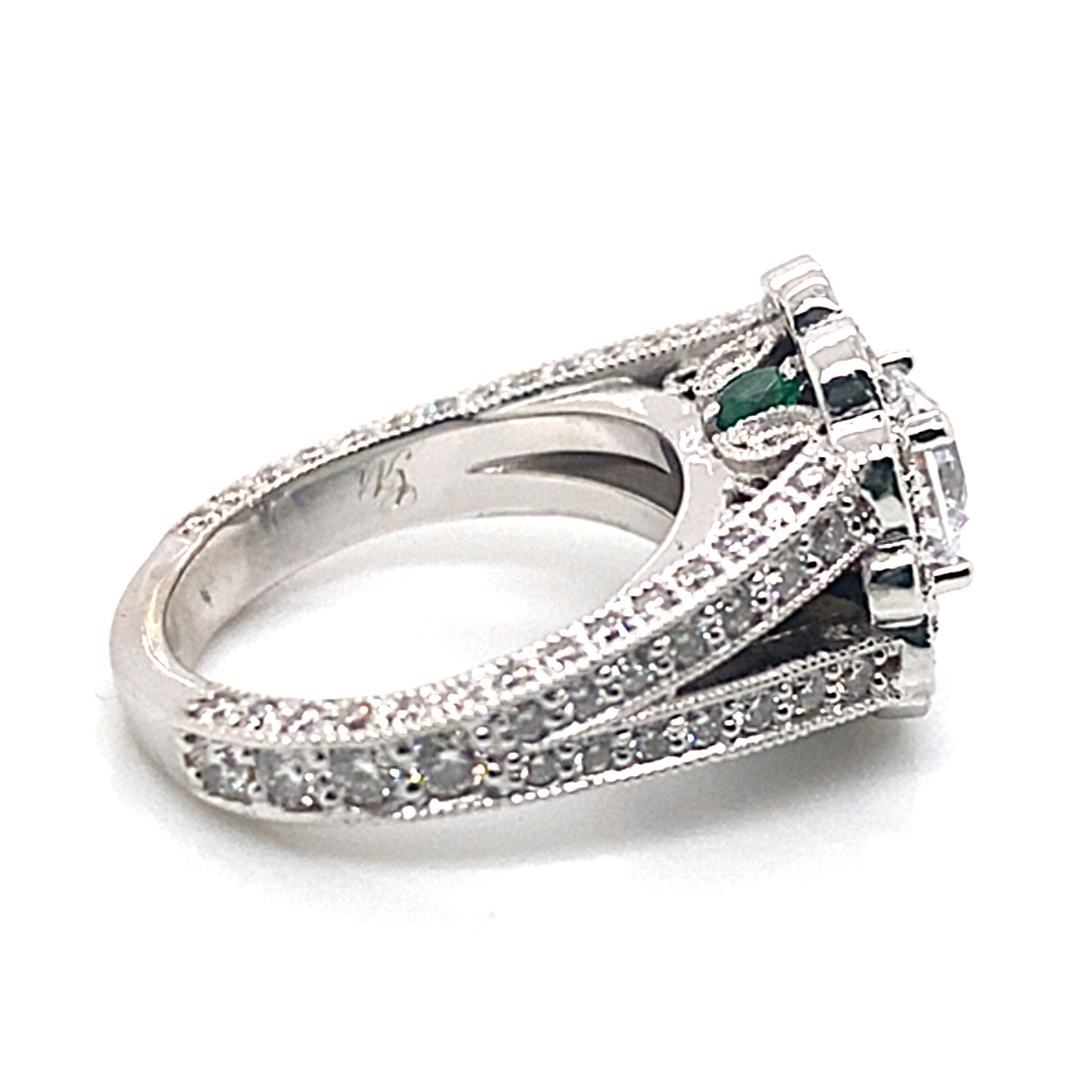 14K white gold ring featuring a 6mm RBC center, surrounded by natural round brilliant diamonds totaling 1.75 carats and accentuated with .25 carats of natural emeralds, all set in a captivating halo design.