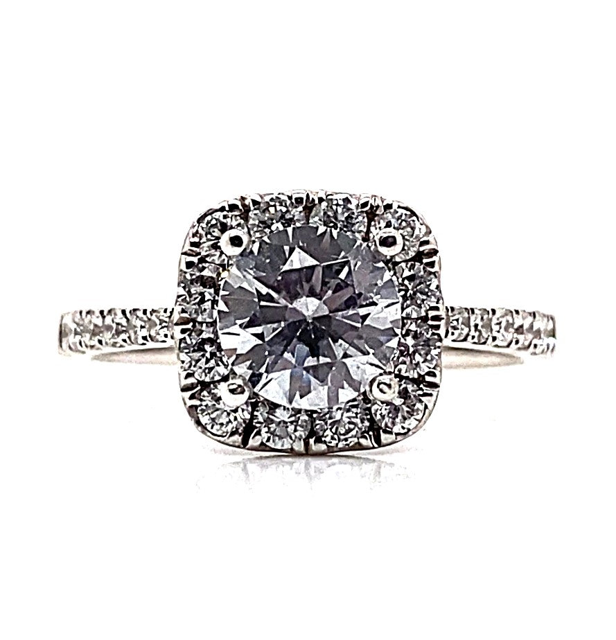 This exquisite engagement ring, crafted in 18K white gold, highlights a dazzling 6.5 mm center stone in a cushion halo setting and is beautifully accented with .59 carats total weight of natural round brilliant diamonds adorning the band.