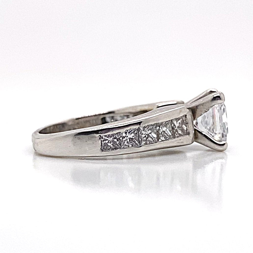 This elegant proposal piece is a captivating 14K white gold engagement ring, showcasing a 6.5 mm center stone and adorned with natural princess diamond accents in a channel set cathedral style along the band.