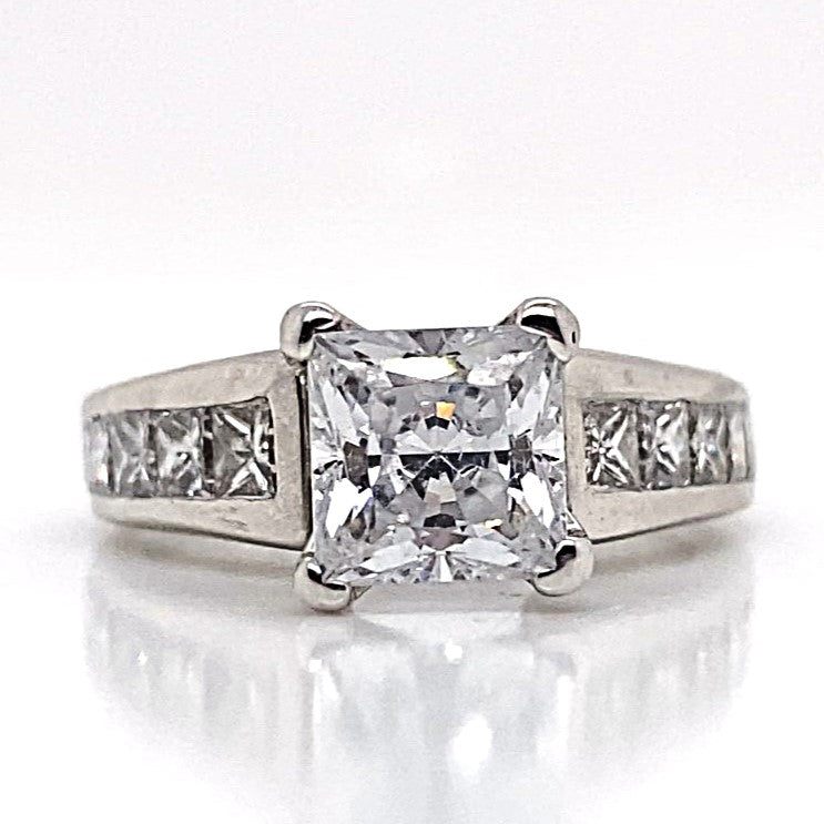 A refined proposal suggests opting for a 14K white gold ring featuring a central 6.5 mm princess-cut diamond and natural princess diamond accents, elegantly arranged in a channel set cathedral style.