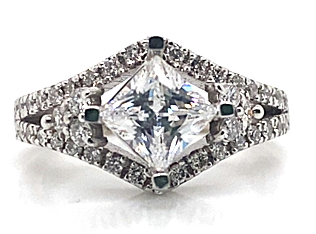 This exquisite engagement ring, known as the 14K White Gold CZ Center (6mm Princess) .85 ct tw Natural Round Brilliant Diamond Accent Ring with a Square Shank, showcases a square center stone set in 14K white gold and features stunning diamond accents that grace the band.