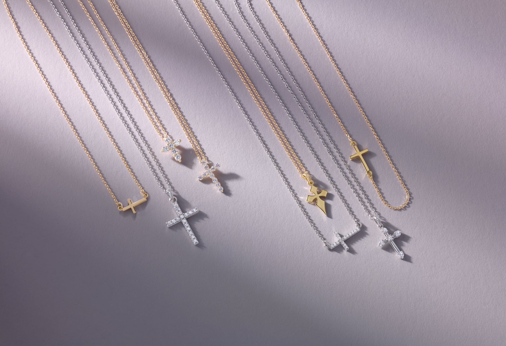 Gold and silver cross necklaces arranged neatly on a light purple surface with soft shadows.