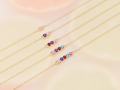 Gold necklaces with colorful gemstones on a soft pink background