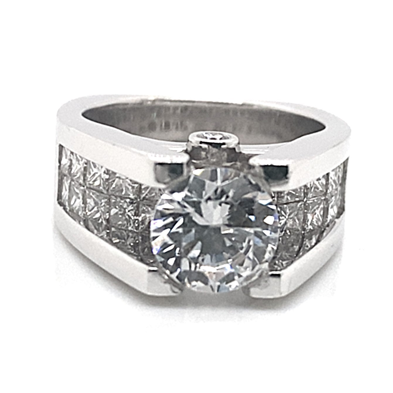 A beautiful 14K white gold engagement ring showcasing an 8.5mm round brilliant cut CZ center stone, complemented by a total of 2.60 carats of natural cut accents and two rows of princess cut stones set invisibly along the band with a cathedral setting.