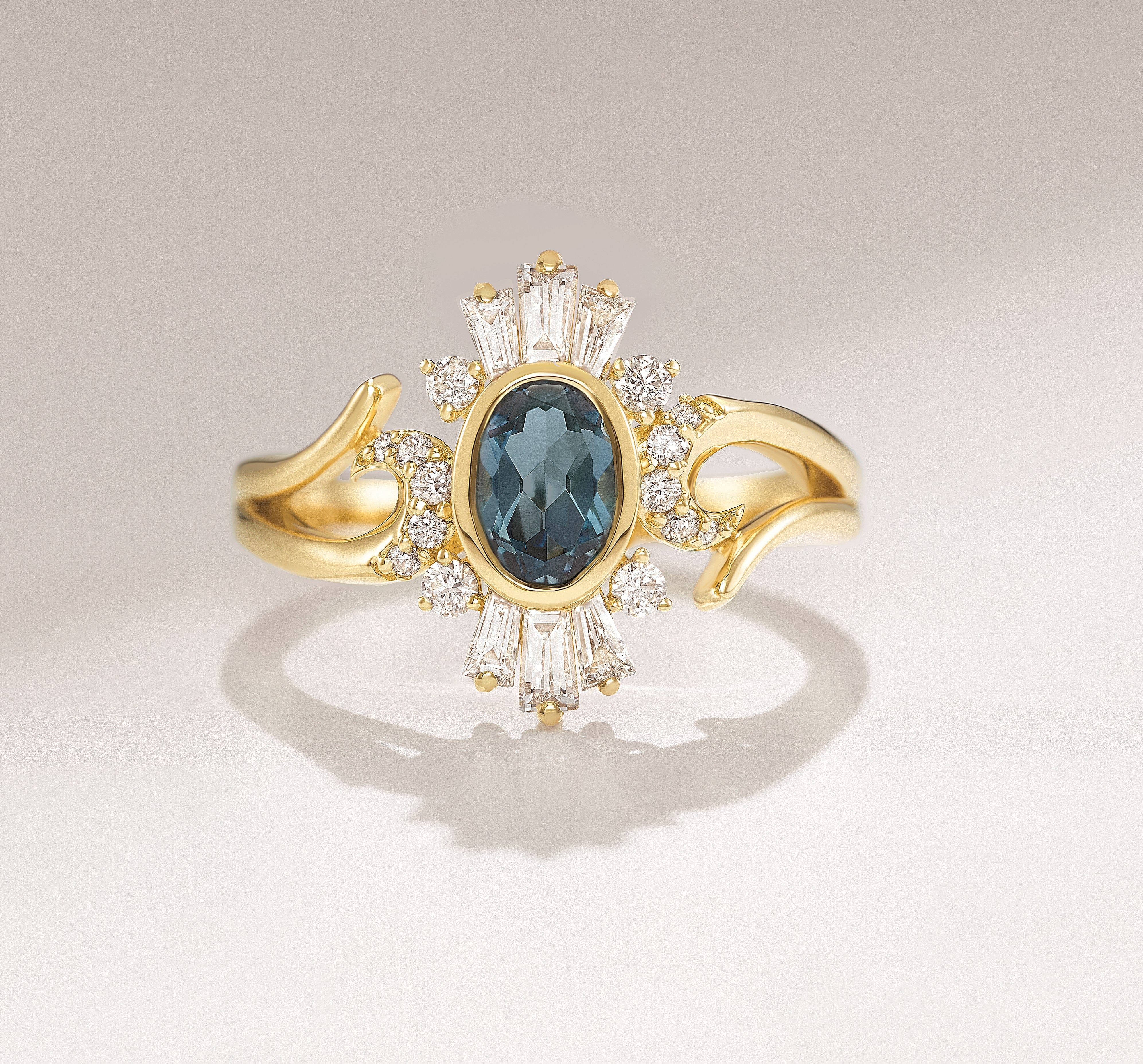 Gold ring with an oval blue gemstone, surrounded by clear diamonds and elegant, swirling band details.