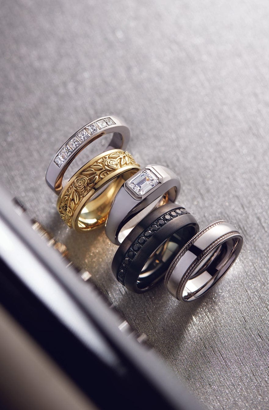 5 unique modern mens wedding bands laying on a gray surface.