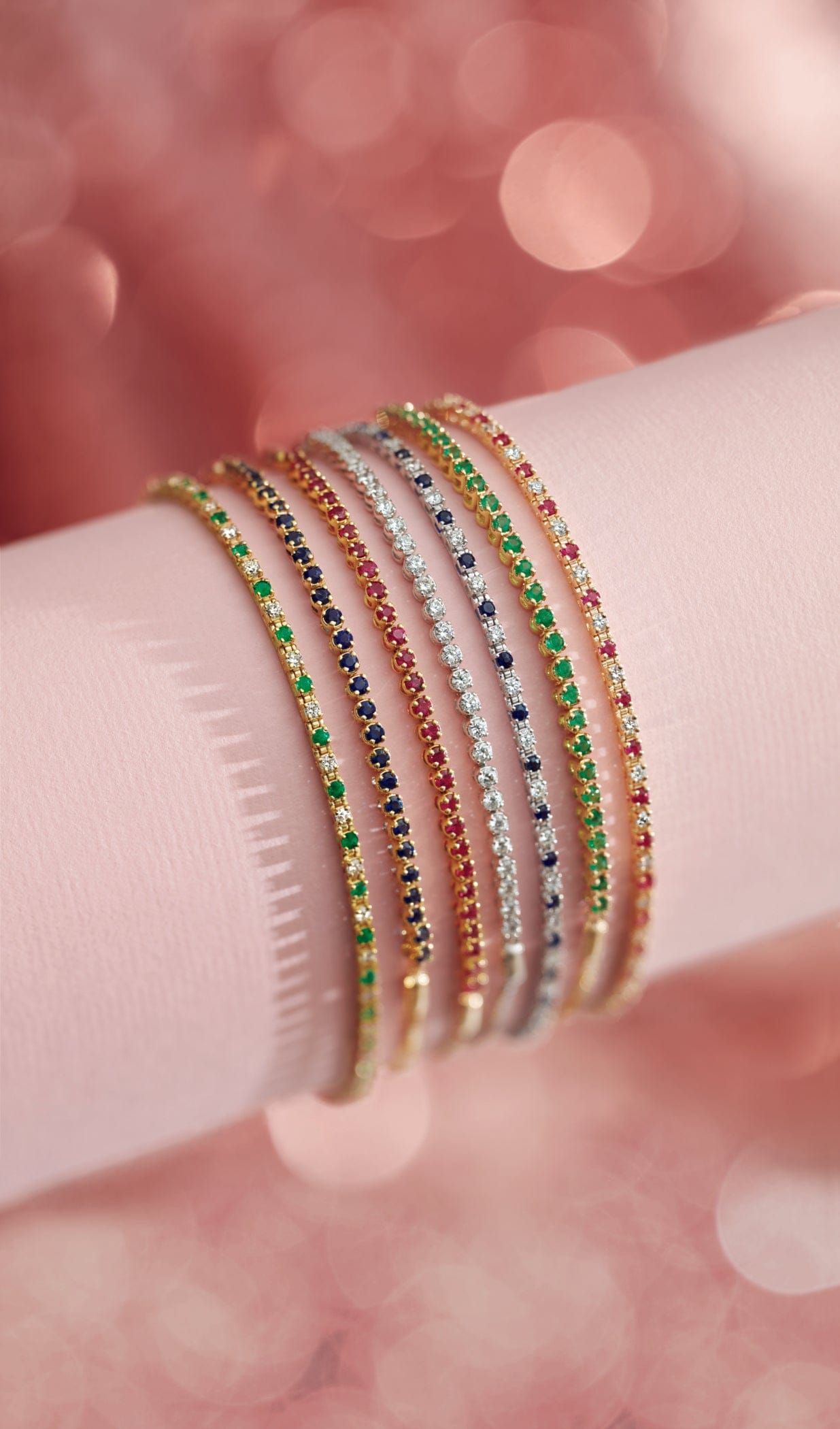 Close-up of a wrist wearing multiple gemstone bracelets with a blurred pink background