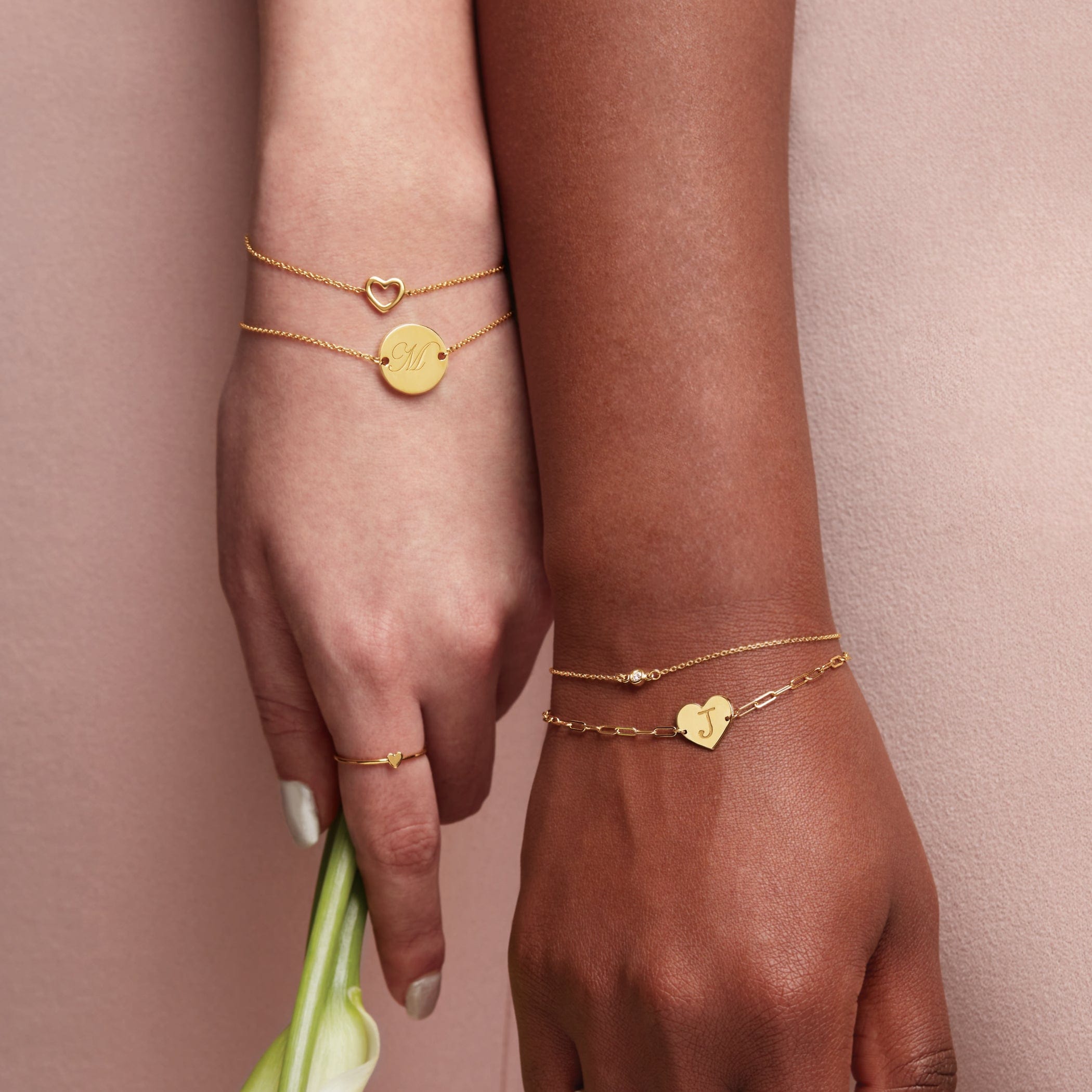 Two hands wearing gold bracelets on a pink background
