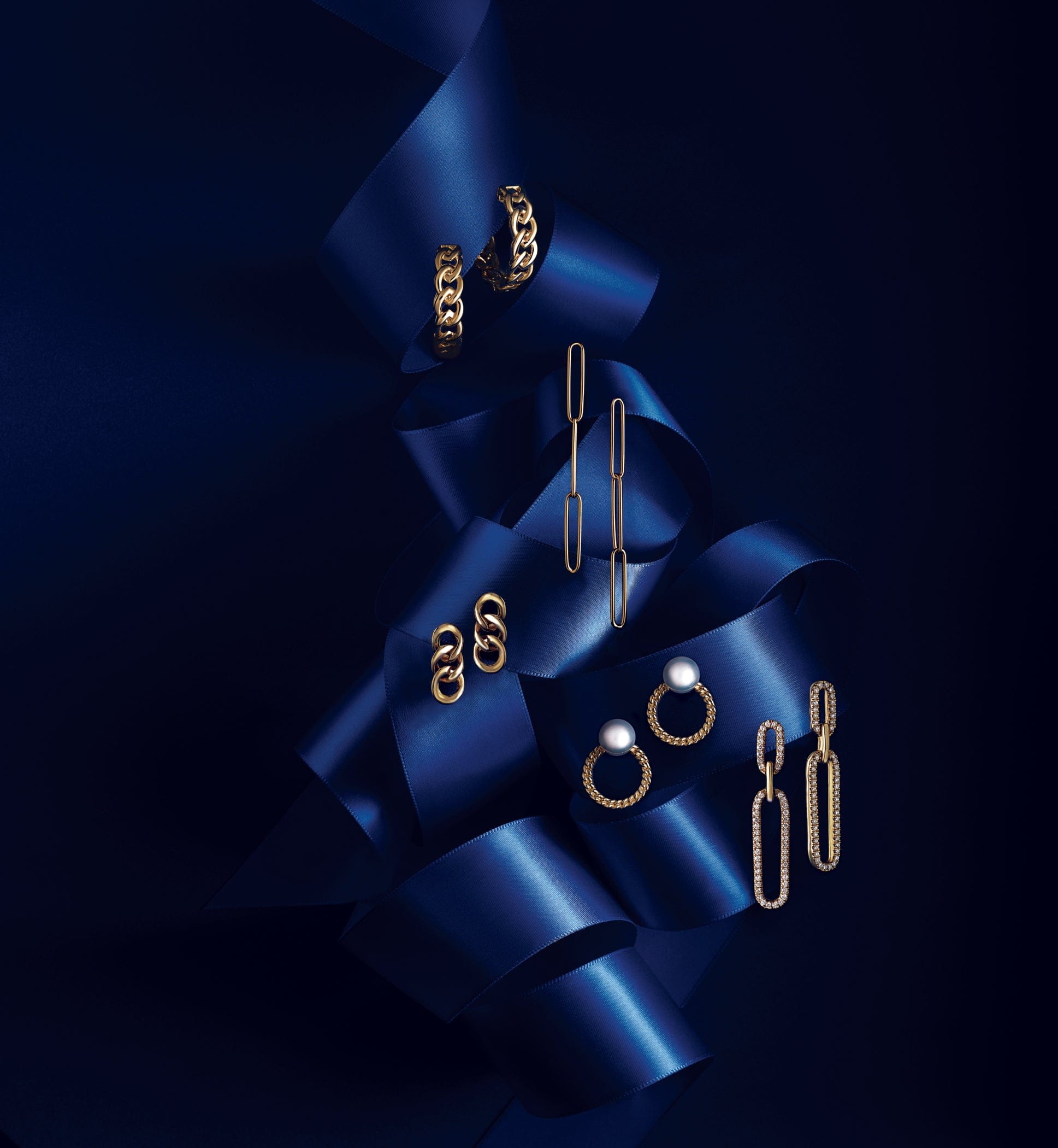 variety of 18k Gold ladies earrings displayed on a dark blue ribbon against a black background