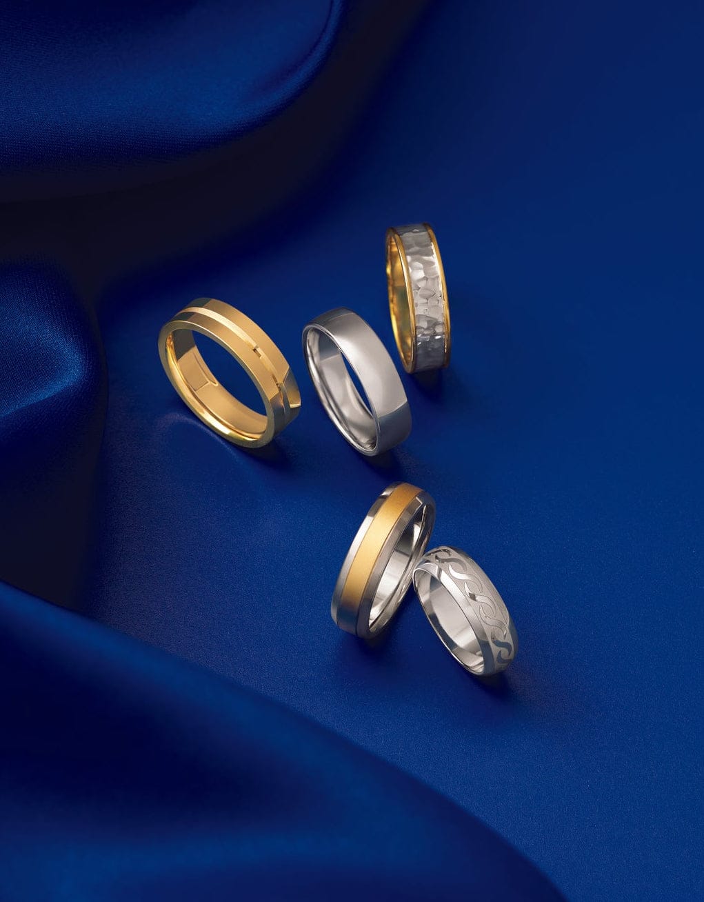 5 unique men's wedding bands laying on a blue silk fabric