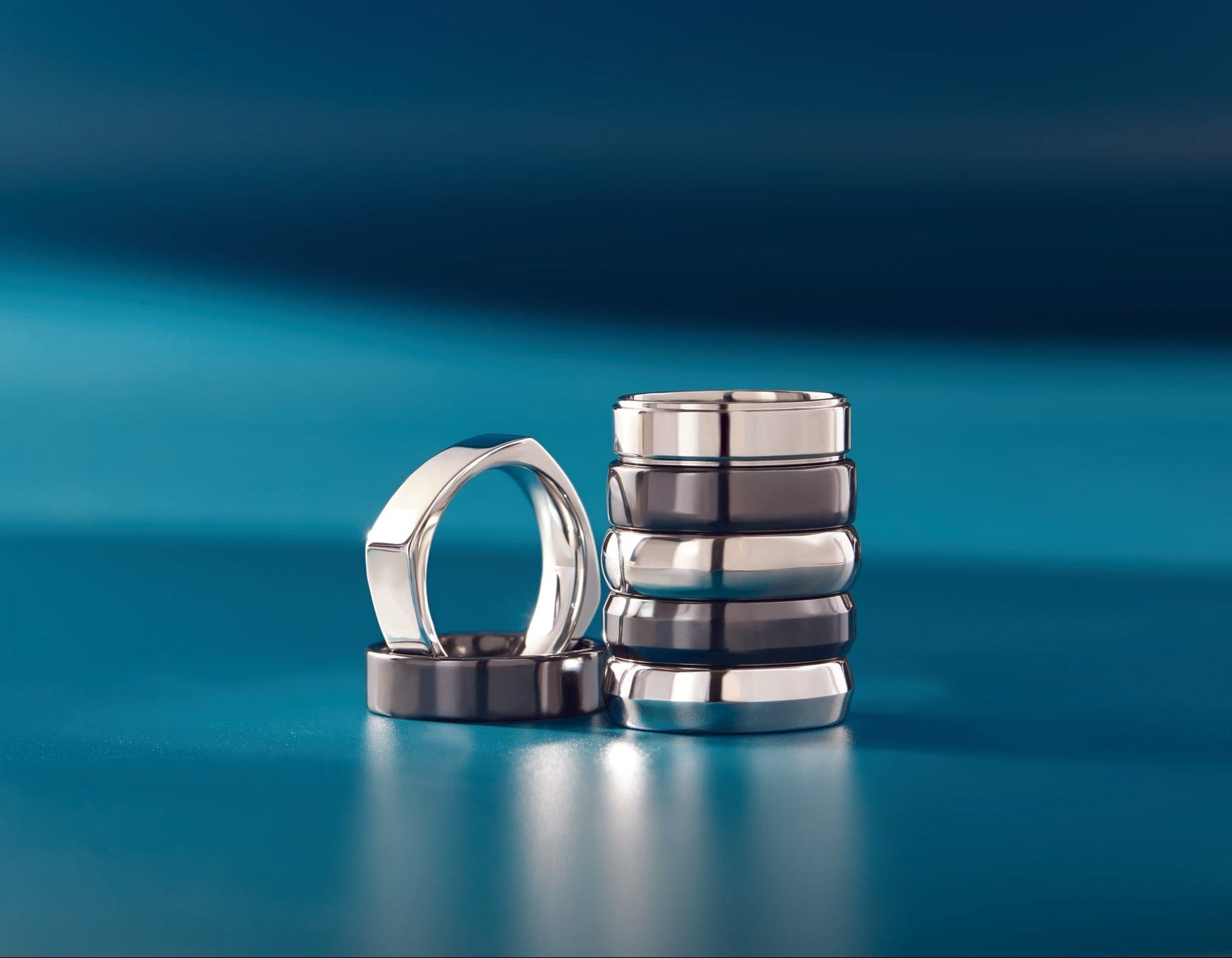 7 modern mens wedding bands on a blue surface