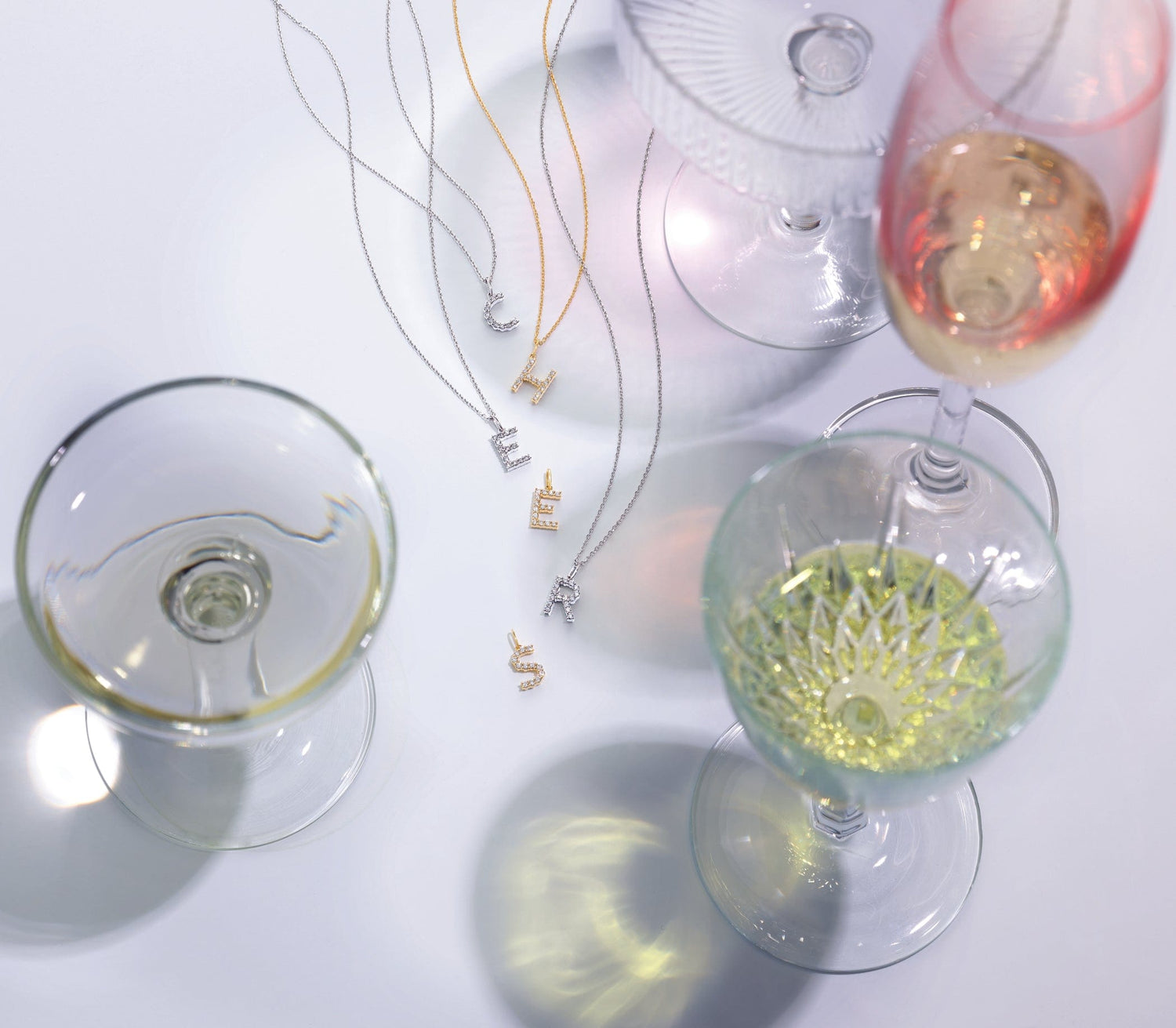 Decorative wine glasses with colorful liquids and fashion necklaces on a light background