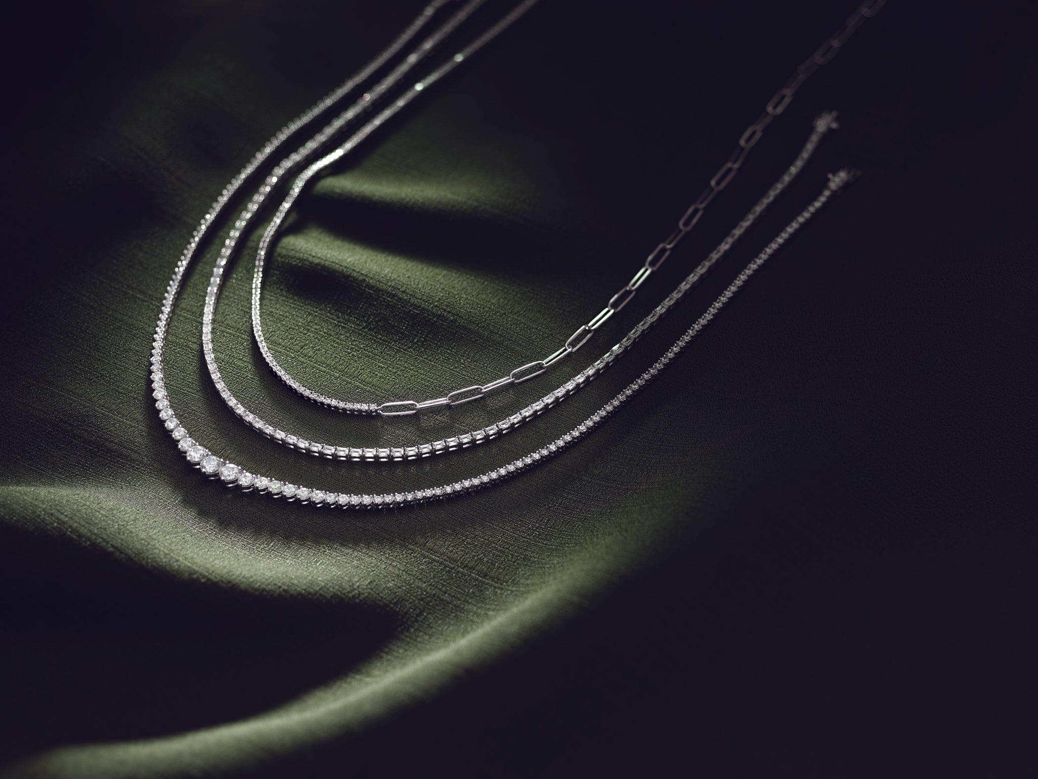 white gold tennis necklaces on a green fabric background