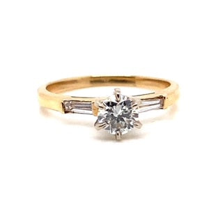 This stunning ring, named the 14K Yellow Gold .50 CT Natural Round Brilliant Diamond Center I/SI1 with .15 CT TW Natural Baguette Diamond Accent, showcases a round SI1 clarity center diamond set in 14K yellow gold, enhanced by elegant baguette diamond accents.