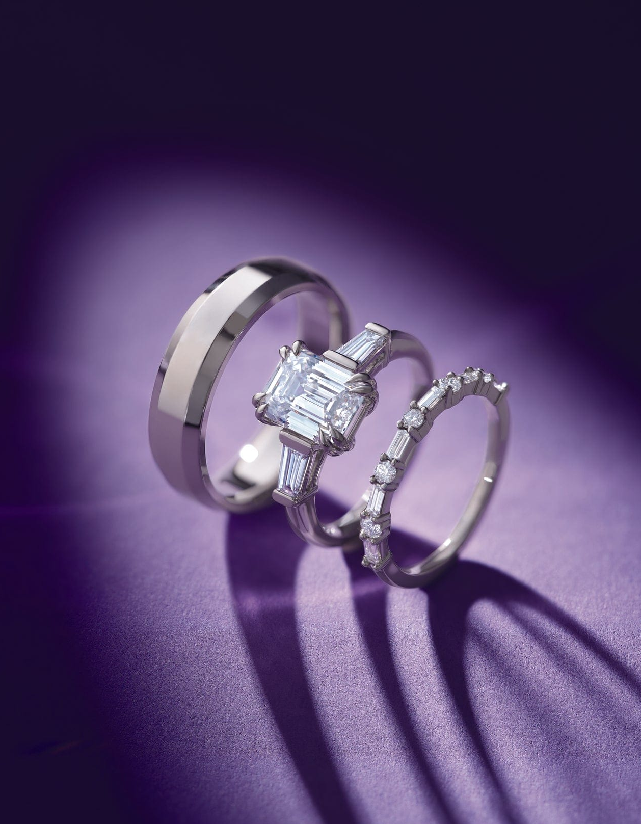 Two white gold rings with diamond accents on a purple background