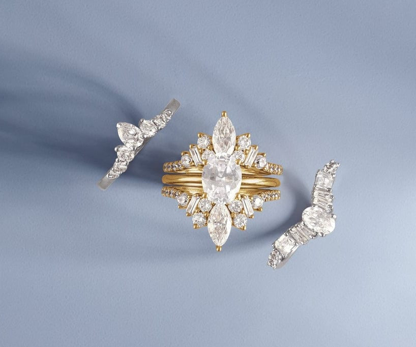 Gold lab grown diamond engagement ring with diamond accents and two matching earrings on a light blue background