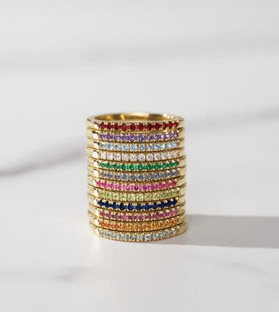 Stack of colorful gemstone rings on a light gray background
