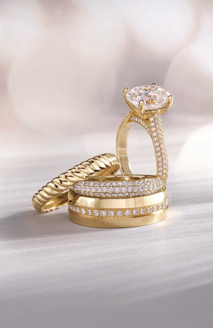 several yellow gold engagment rings with lab diamond accents on a soft, blurred background