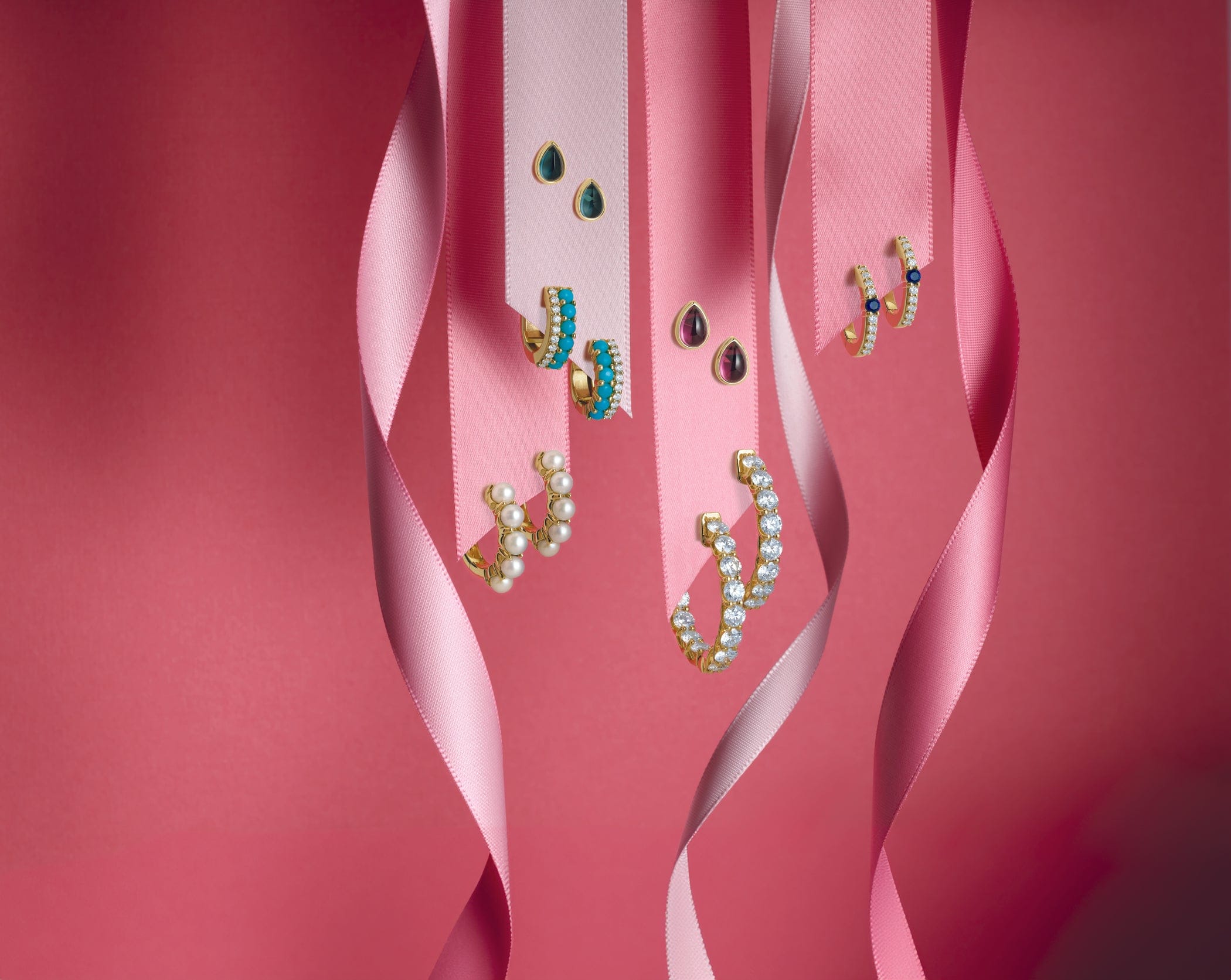 Jewelry set with gemstone earrings on pink ribbons against a pink background