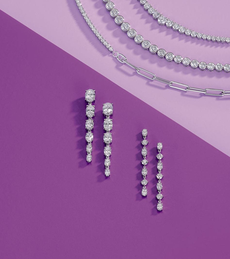 Jewelry set including diamond tennis necklaces and diamond drop earrings on a purple background