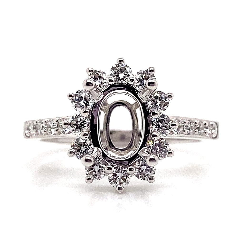 This 18K white gold halo style ring, adorned with .62 ct tw natural round brilliant diamond accents, elegantly frames an 8x6 mm oval center stone space, making it ideal for a memorable proposal.