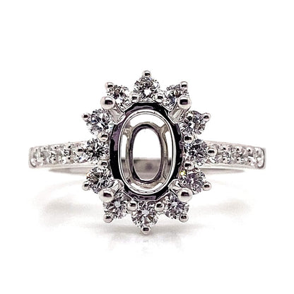 This 18K white gold halo style ring, adorned with .62 ct tw natural round brilliant diamond accents, elegantly frames an 8x6 mm oval center stone space, making it ideal for a memorable proposal.