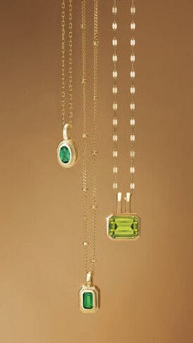 Three green gemstone pendants on gold chains against a brown background