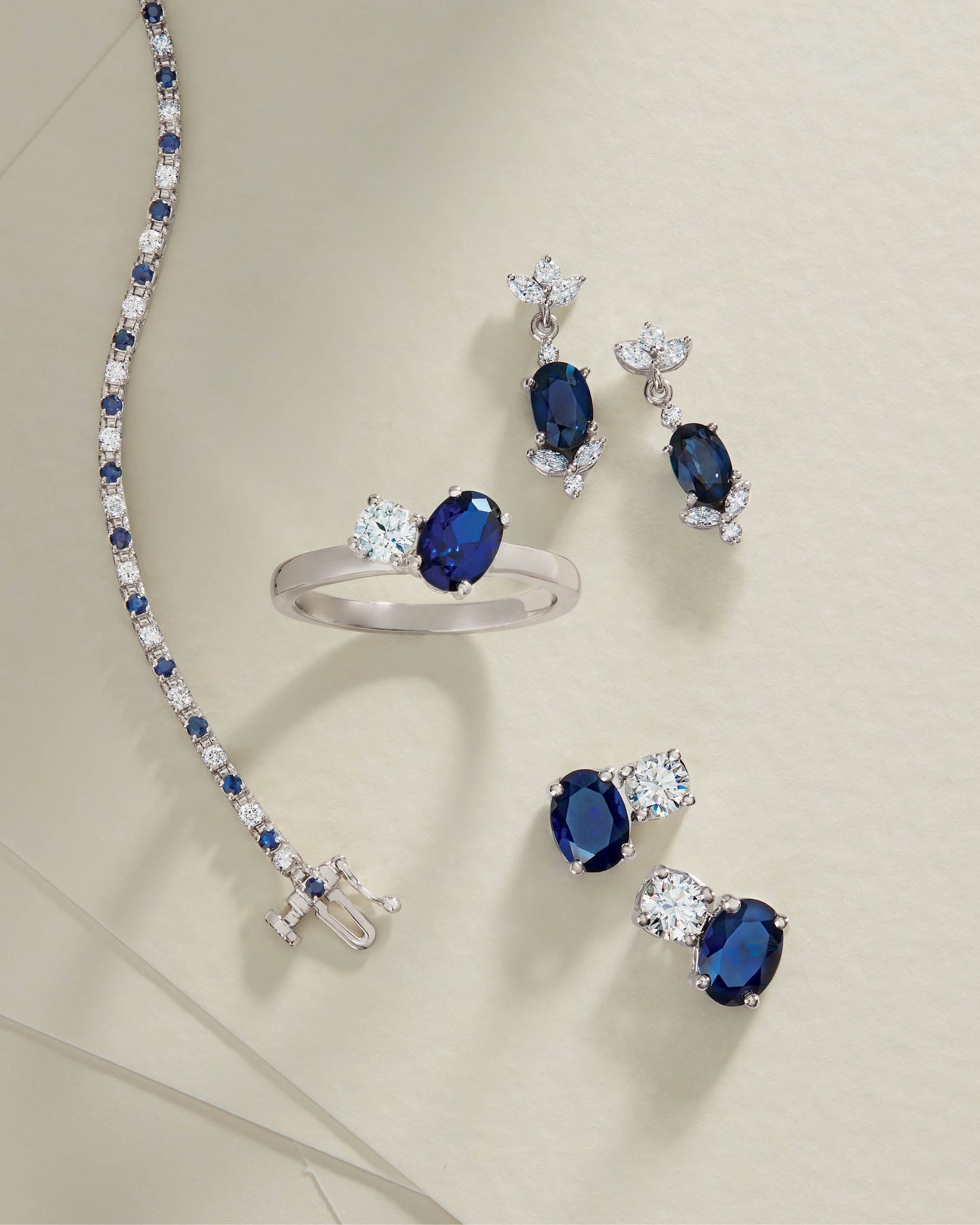 Sapphire and diamond bracelet, ring, and earrings displayed on a cream-colored surface.