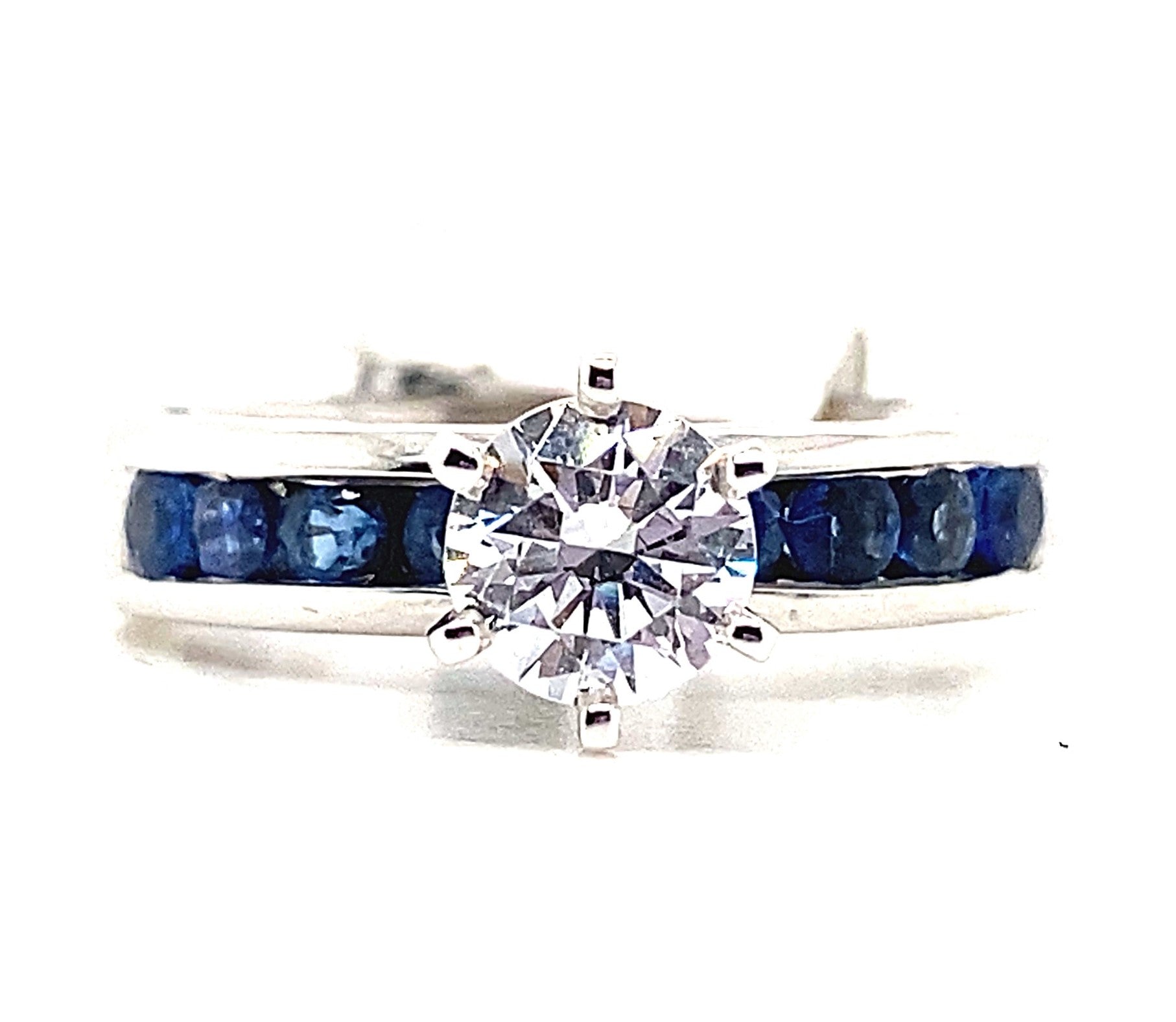 Explore the elegance of a 14K white gold ring showcasing a stunning central cubic zirconia (6.5mm, .70 ct total weight) and adorned with natural round brilliant blue sapphires in a channel set along the band.