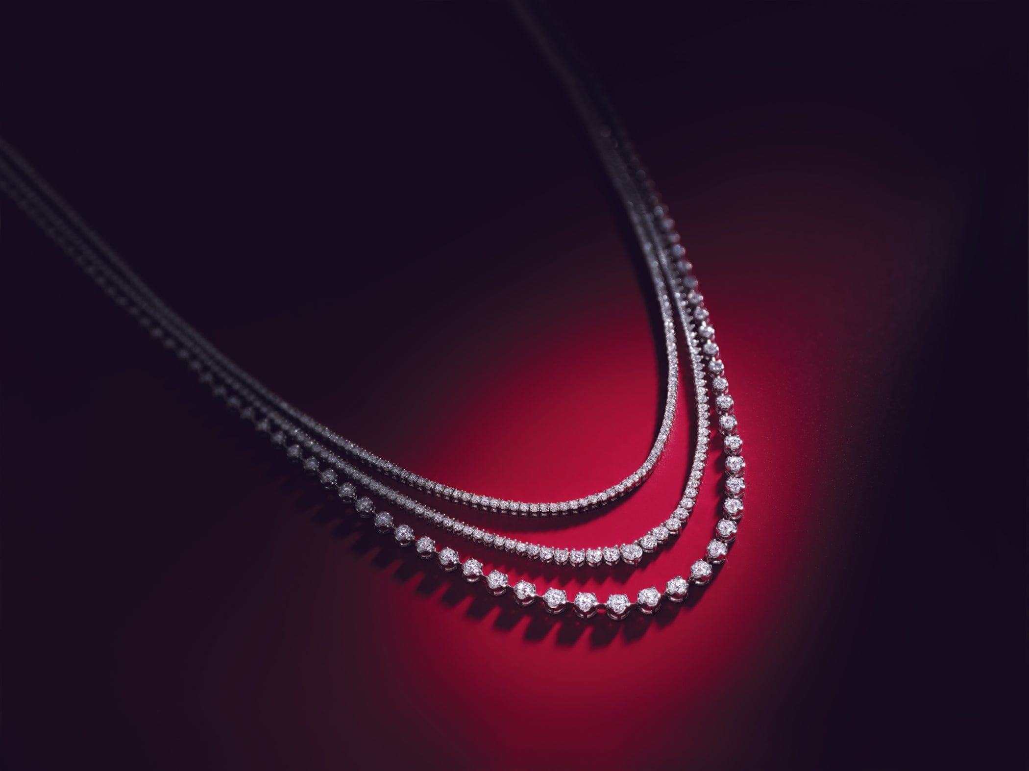 Close-up of a diamond tennis necklace on a dark background with red lighting