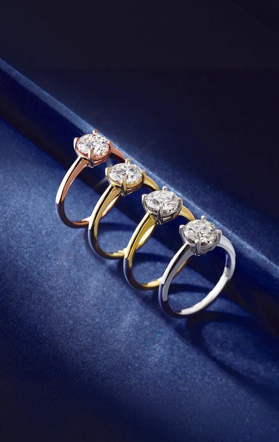 Three diamond-studded engagement rings in rose gold, yellow gold, and white gold on a dark blue background.