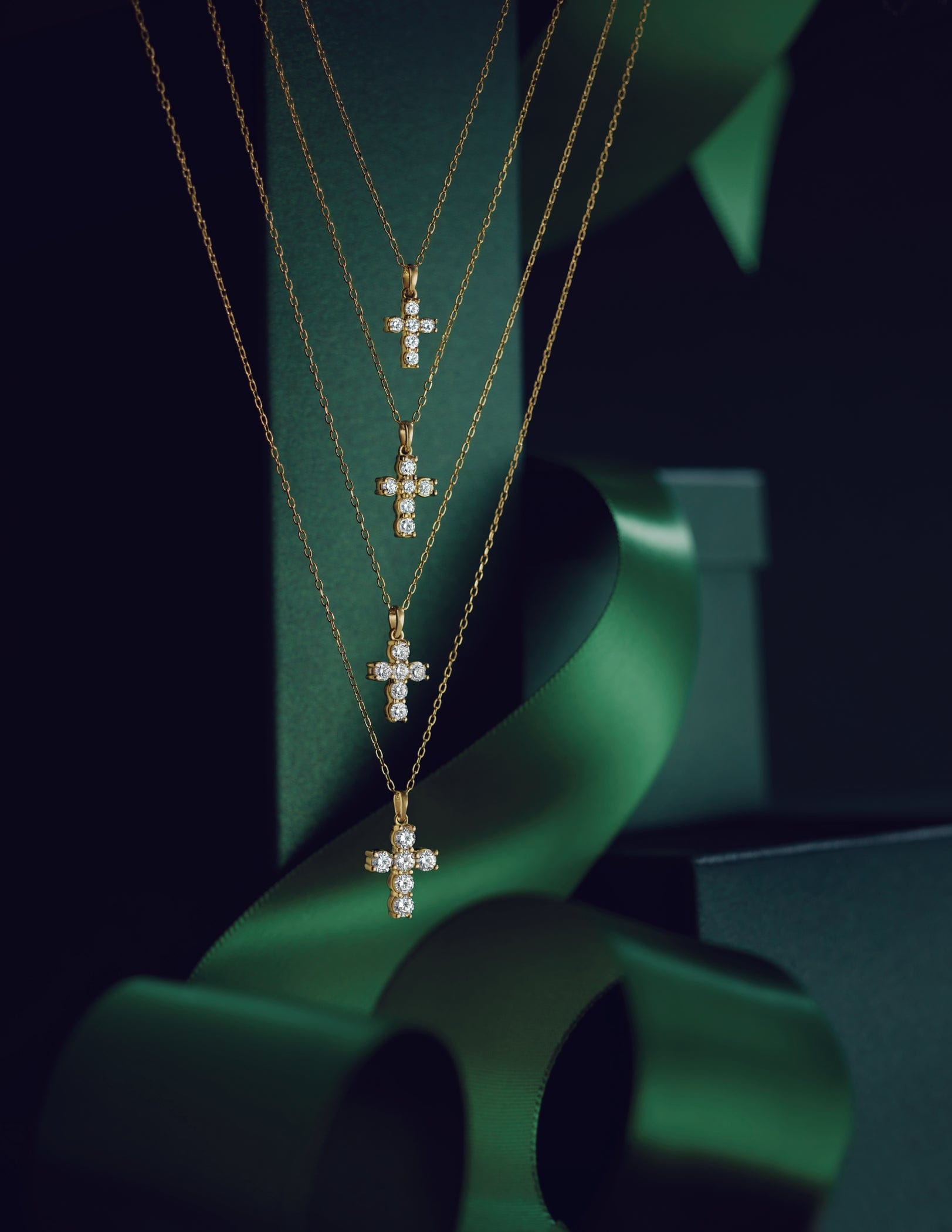 Three gold necklaces with diamond cross pendants on a green background