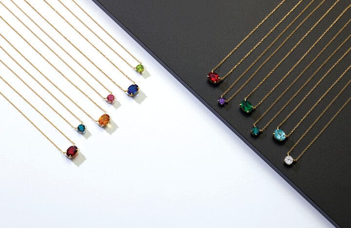 Nine gold necklaces with colorful gemstone pendants displayed on white and black surfaces.