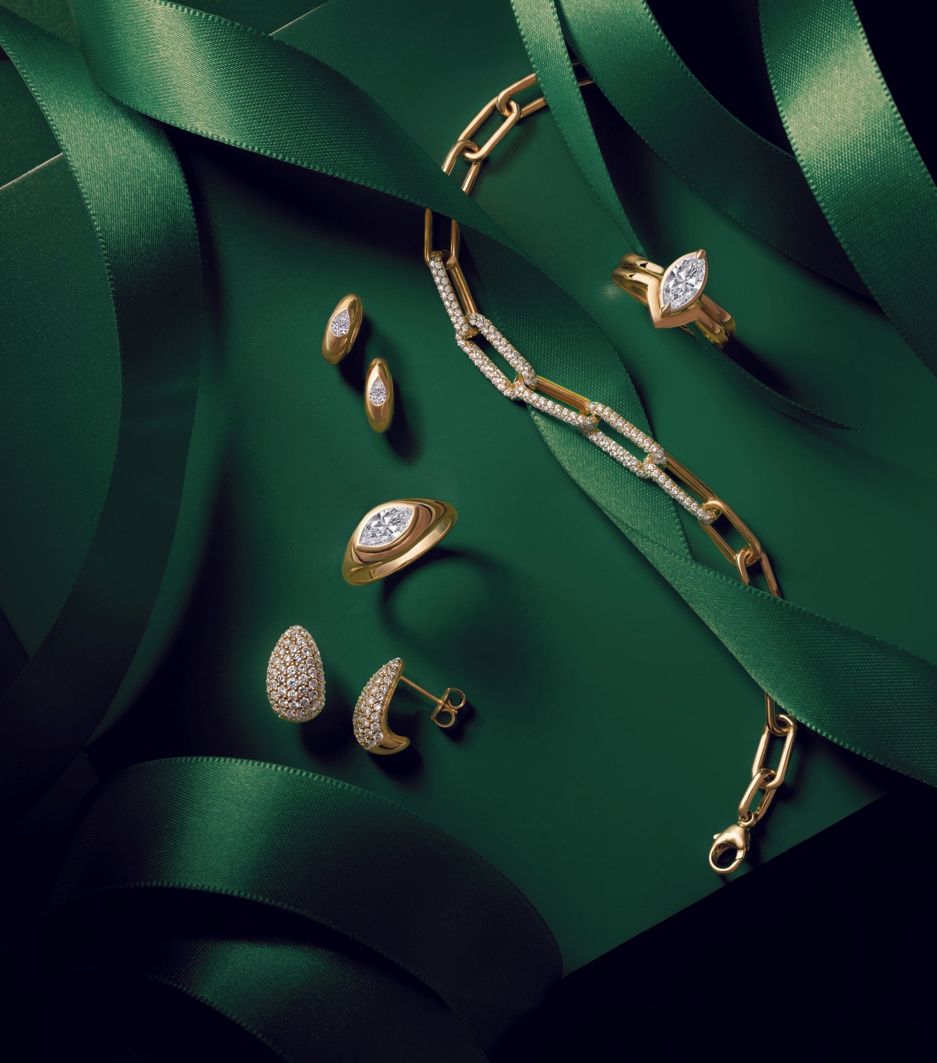 Gold jewelry with diamonds displayed on a green surface, decorated with elegant green ribbons.