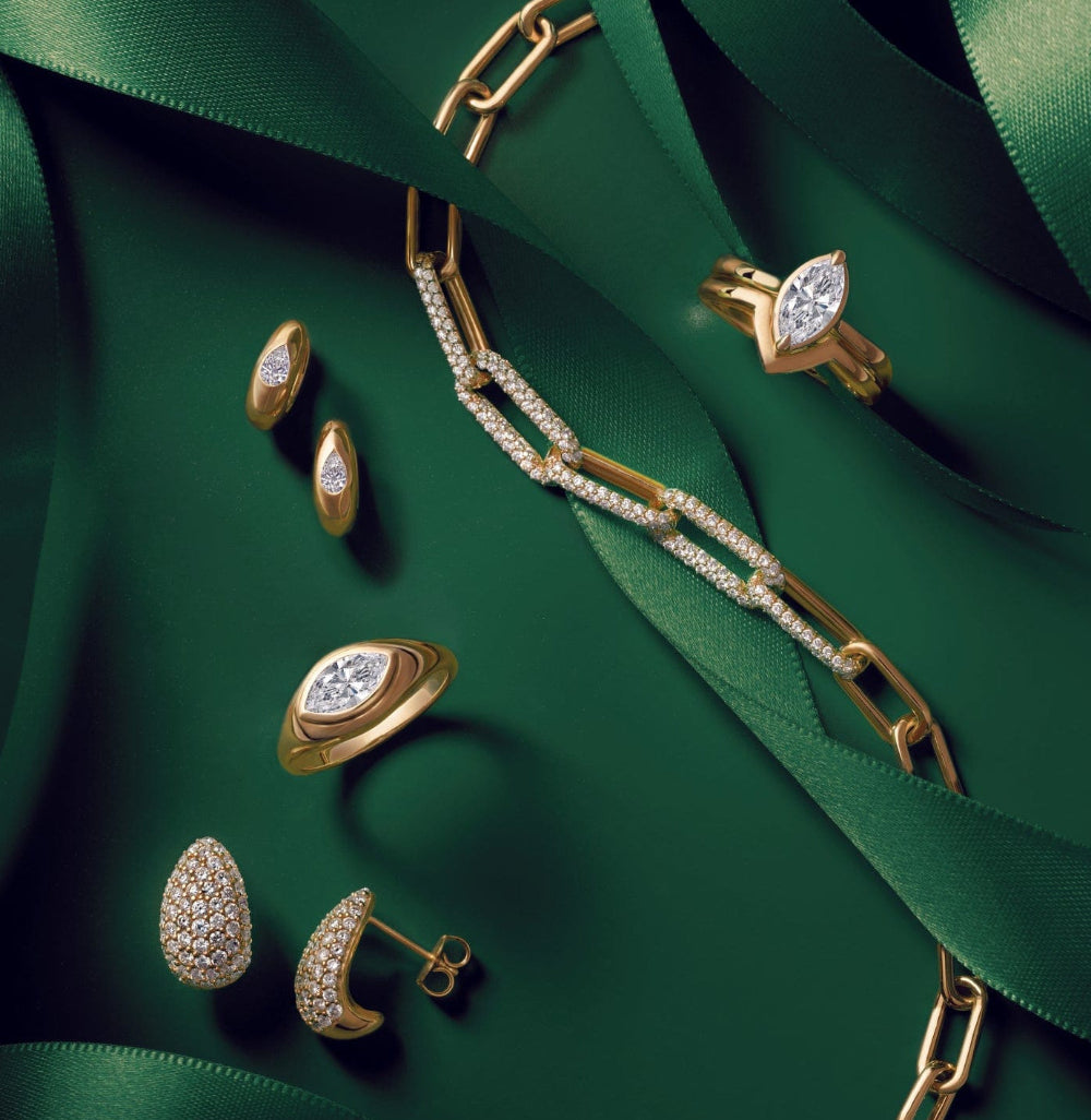 Gold jewelry with diamonds displayed on a green surface, decorated with elegant green ribbons.