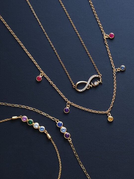 Gold necklaces and bracelets with colorful gemstone charms displayed on a dark background.