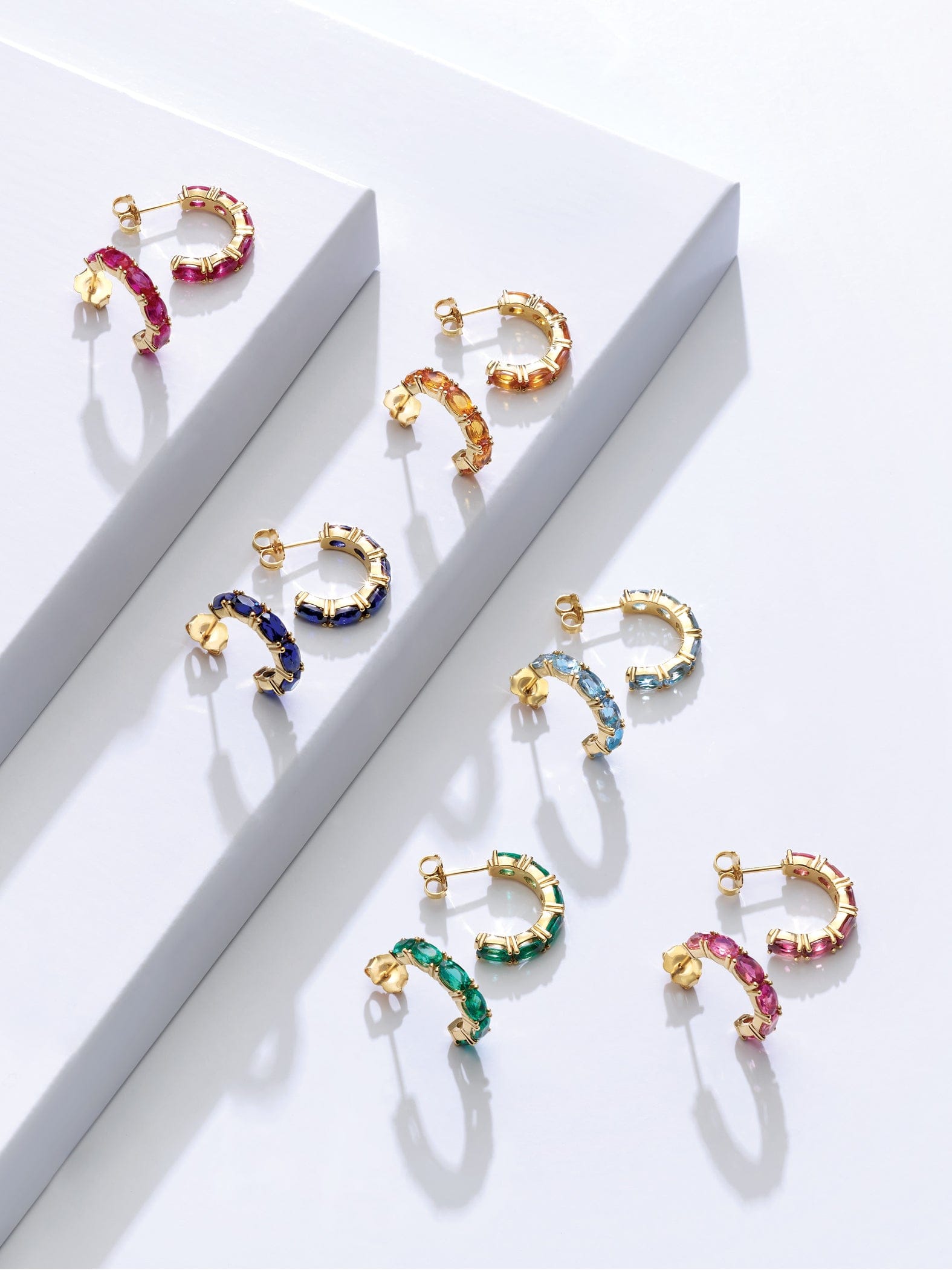 Colorful gemstone hoop earrings on a white surface with a box in the background