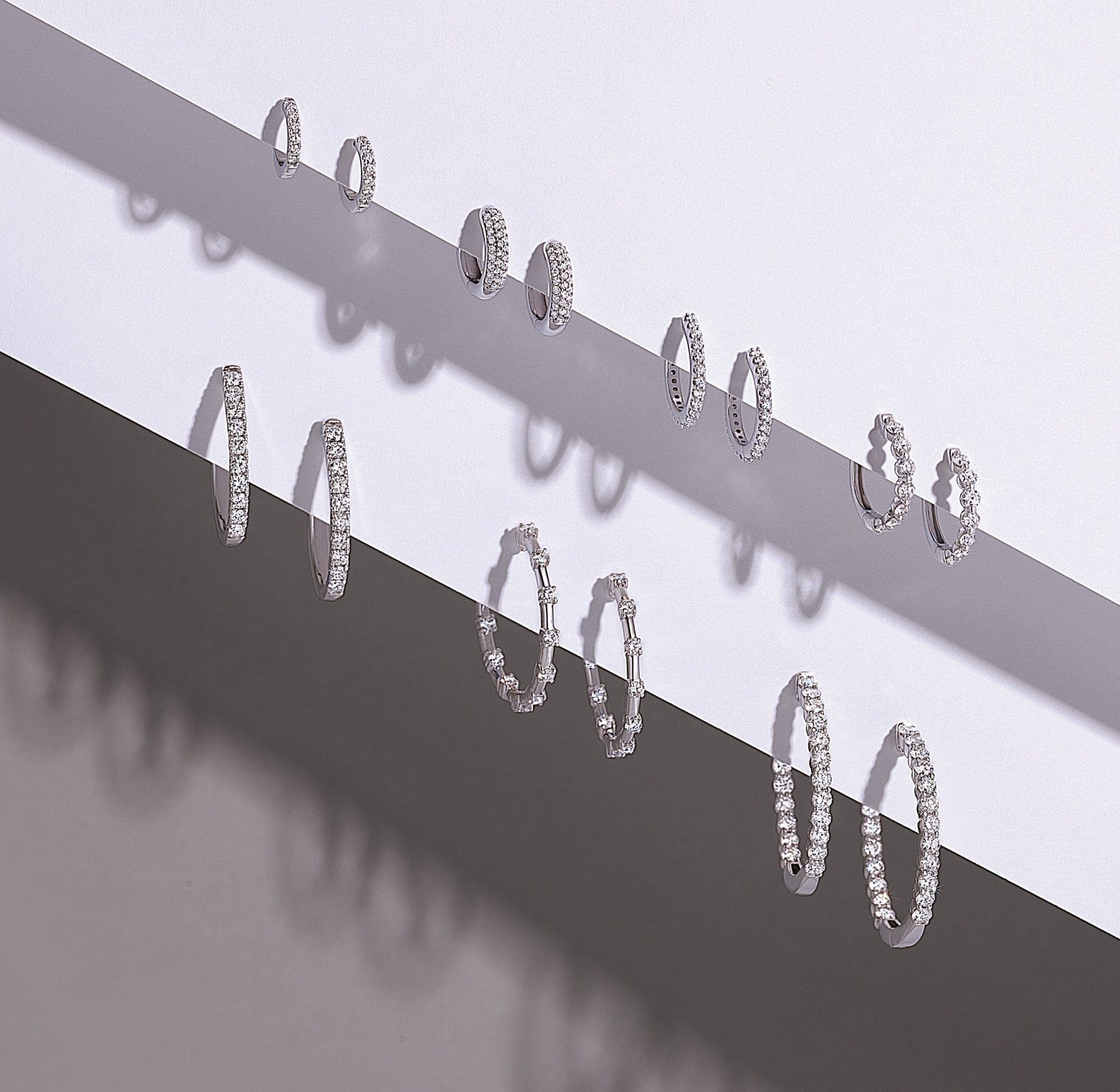 Five pairs of silver hoop earrings in varying sizes and designs displayed on a two-tone background.