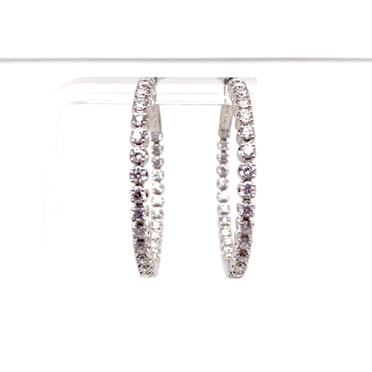 The 18K White Gold 2.24 CT TW Natural Round Brilliant Diamond Accent In and Out Hoop Style Earrings shimmer beautifully, showcased on a clear stand against a pristine white background.