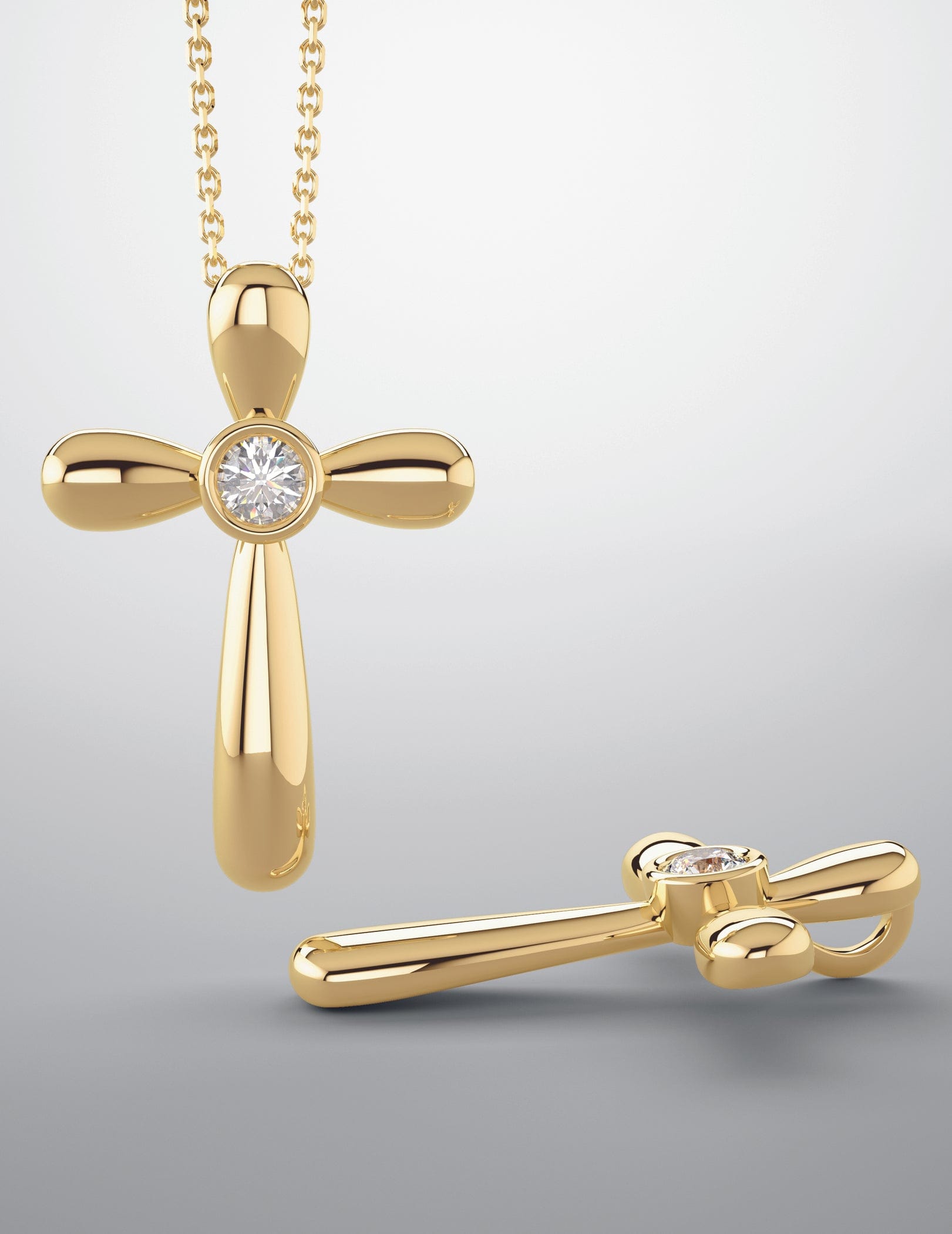 Gold cross pendants with a central diamond, one hanging on a chain and one lying flat on a gray background.