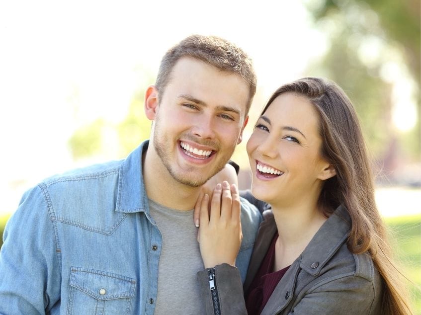 Man and woman smiling outdoors with a blurred natural background