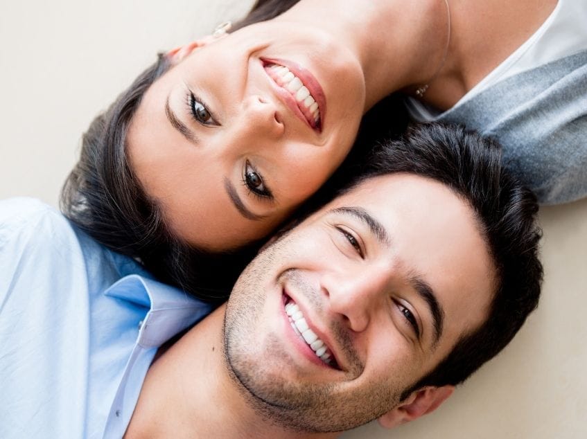 Two people lying down and smiling at each other on a light background