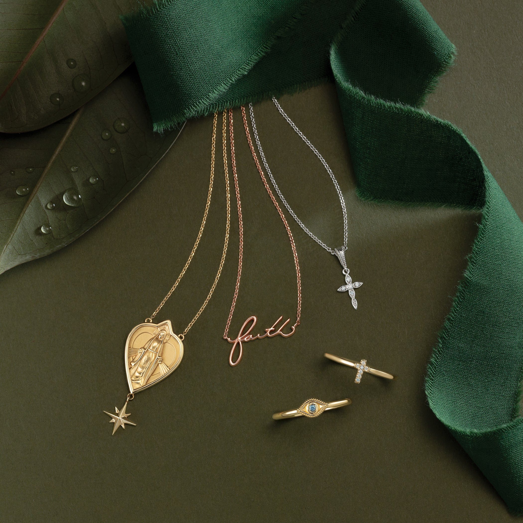 Three necklaces and two rings displayed on a green background with green ribbon and leaves.