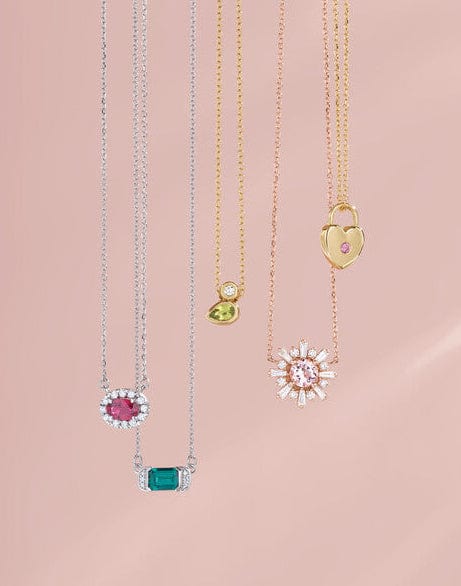 Five delicate necklaces with colorful gemstone pendants hanging against a soft pink background.