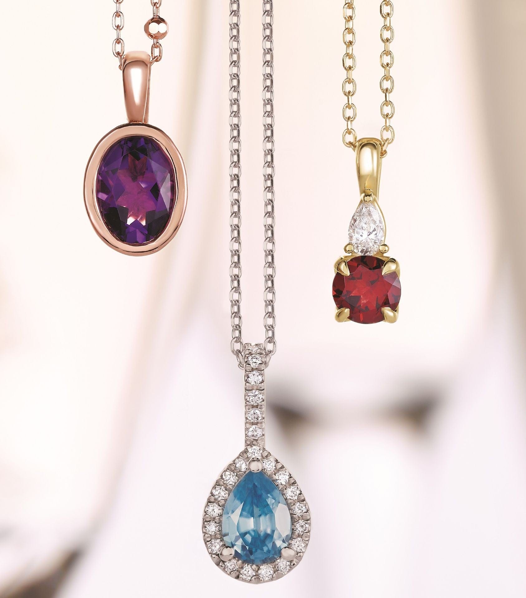Three gemstone necklaces: amethyst in rose gold, blue topaz with diamonds, and ruby with a diamond in yellow gold.