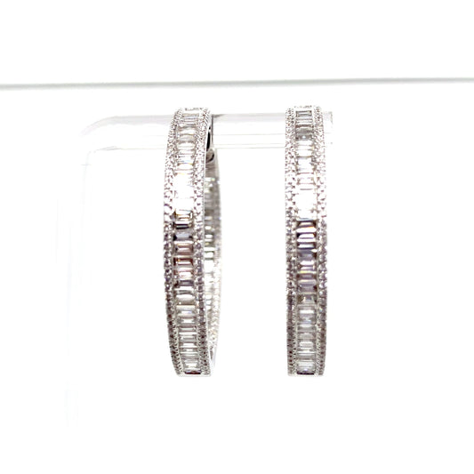 The 18K white gold hoop earrings, featuring a total of 3.57 carats of natural baguette and round brilliant diamond accents, are elegantly displayed on a clear stand against a white background, embodying the essence of luxury jewelry.