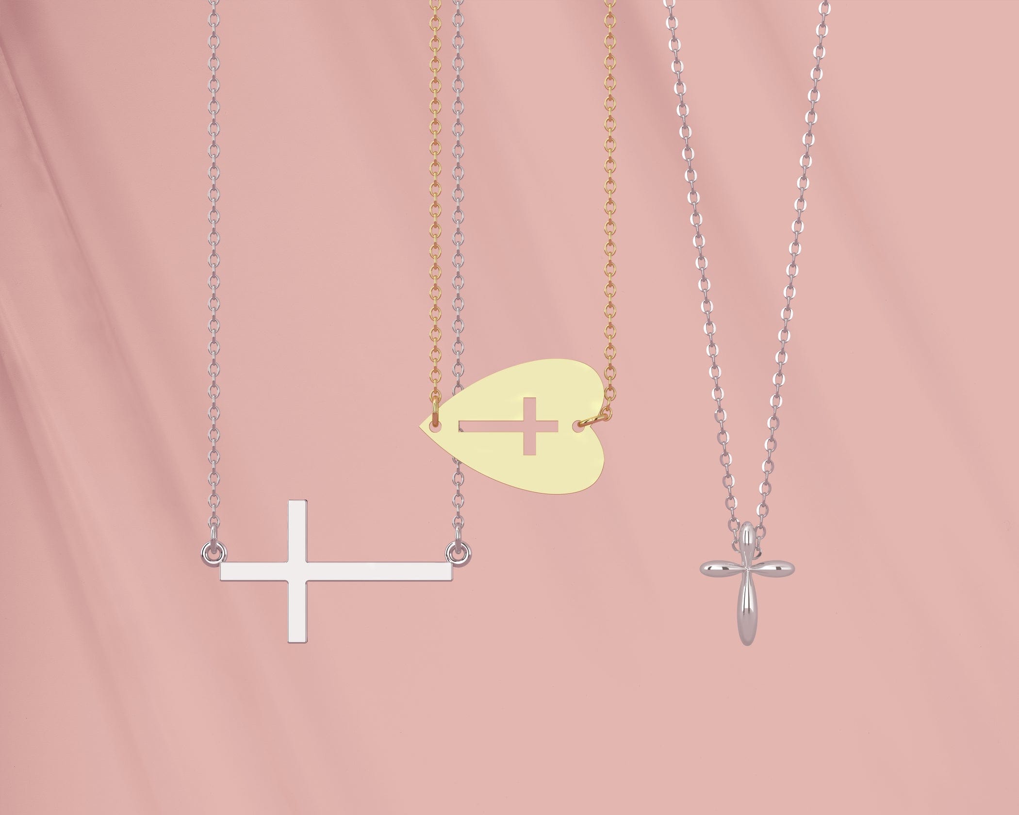 Three necklaces with cross pendants on silver and gold chains against a soft pink background.
